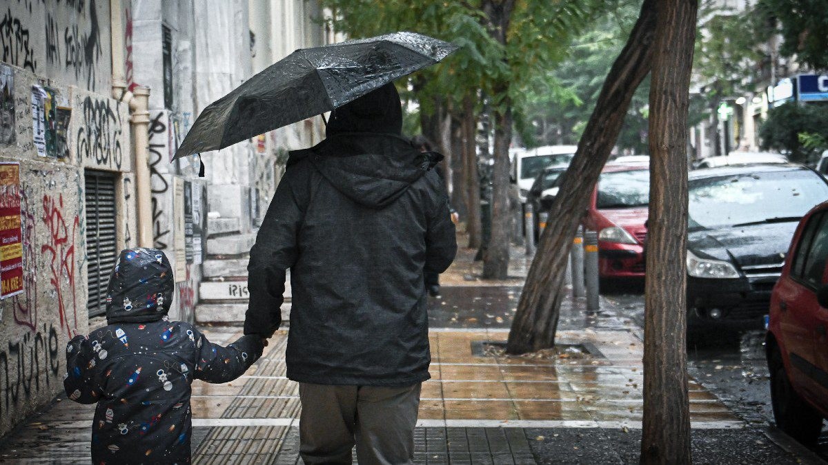 Ένας μπαμπάς με το παιδί του περπατούν στη βροχή