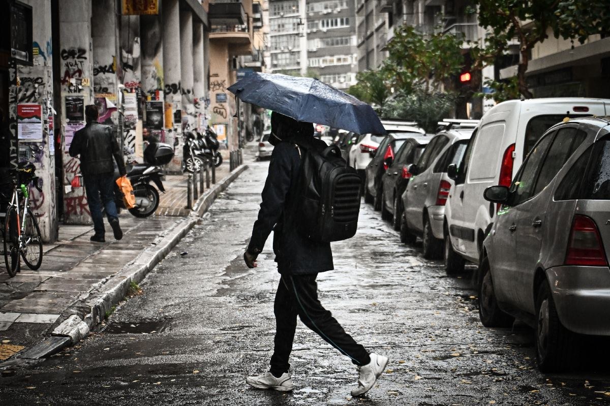 ένας μαθητής περπατάει στην βροχή με ομπρέλα στο χέρι